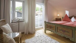 A bedroom with a bed, a small table, a chair, and a window with curtains. - Kaiserblick Comfortable Holiday Residence (Oberaudorf)