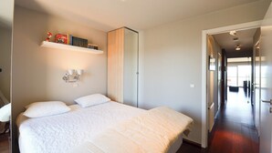 Quarto com cama grande, guarda-roupa, estante com livros e corredor que dá para outro cômodo.