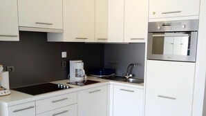 A modern kitchen with white cabinets, a built-in oven, a coffee maker, and a black rug. - Apartment in Nieuwpoort With sea View (Nieuwpoort)