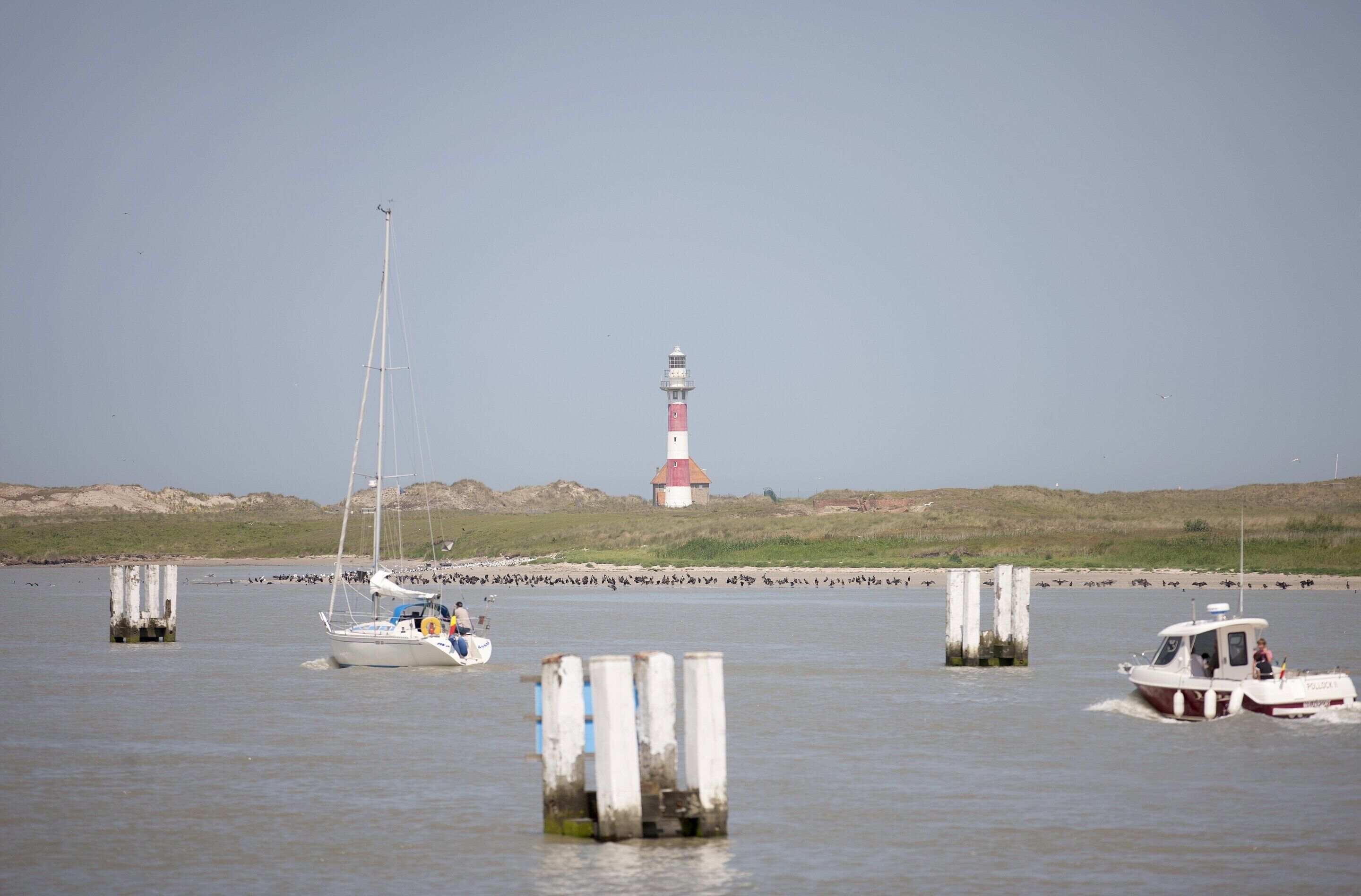 Um farol, um veleiro e um barco a motor em águas calmas.