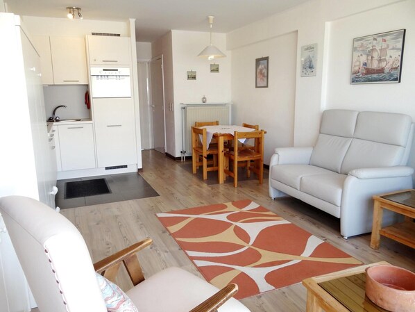 Una sala moderna con un sofá, una mesa de comedor con sillas, una zona de cocina con un refrigerador y una alfombra estampada.