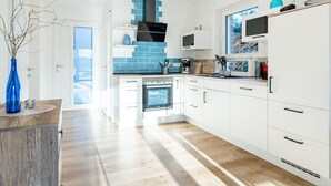 A modern kitchen with white cabinets, a blue backsplash, and a built-in oven. - Nitschke - Vakantiewoning Watt (Aurich)