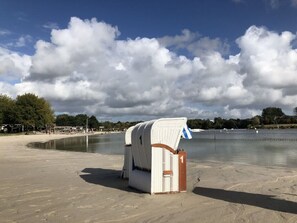 A beach with a white beach chair and a towel, a calm lake, and a cloudy sky. - Nitschke - Vakantiewoning Watt (Aurich)