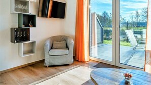 A modern living room with a grey armchair, a flat-screen TV, and built-in shelving with glassware. - Nitschke - Vakantiewoning Watt (Aurich)