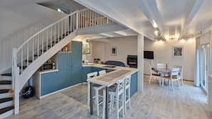 A modern kitchen with blue cabinets, a dining area with white chairs, and a staircase with white railings. - Ferienhaus in Hellenthal, Eifel (Hellenthal)