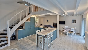 A modern kitchen with a central island, a dining area with a table and chairs, and a staircase leading to an upper level. - Ferienhaus in Hellenthal, Eifel (Hellenthal)
