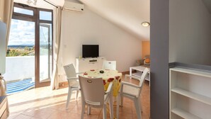 Uma área de refeições com mesa, cadeiras, televisão e varanda com vista.