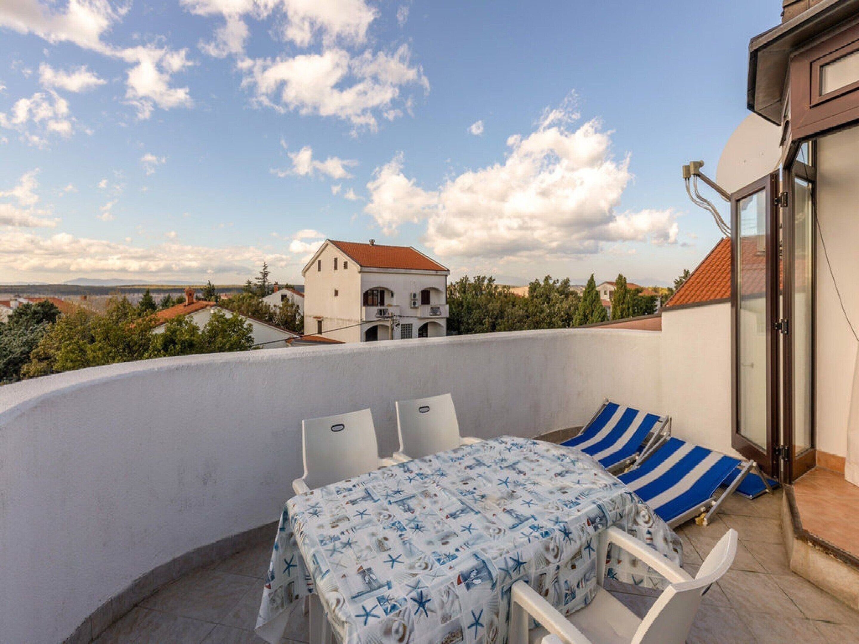 A balcony with a table and chairs, a striped cushion, and a view of a white building in the distance.