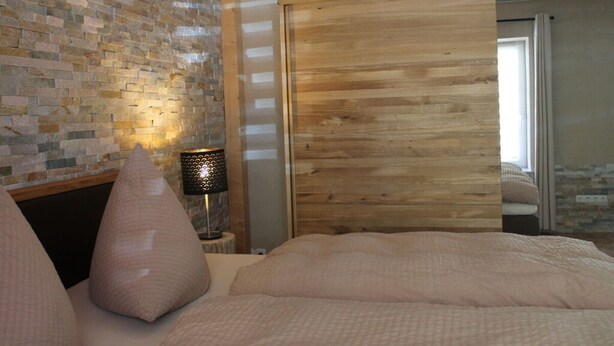 A bedroom with a brick wall, a wooden door, and a bed with pillows.