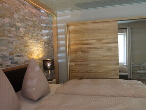 A bedroom with a brick wall, a wooden door, and a bed with pillows. - Plush Apartment in Annaberg-buchholz (Annaberg-Buchholz)