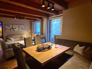 A cozy dining area with a wooden table, chairs, and a sofa. There are wall art pieces and a window with a view. - Plush Apartment in Annaberg-buchholz (Annaberg-Buchholz)