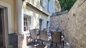 An outdoor patio with a table and chairs, a stone wall, and a building in the background.