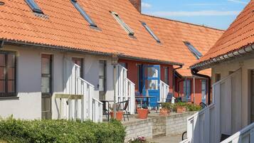 A row of traditional houses with red-tiled roofs and white walls, featuring a central building with a blue door and a staircase leading to a covered porch.