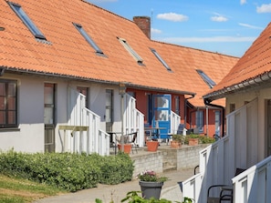 Une rangée de maisons traditionnelles aux toits de tuiles rouges et aux murs blancs, avec un bâtiment central doté d’une porte bleue et d’un escalier menant à un porche couvert.
