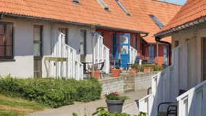A row of traditional houses with red-tiled roofs and white walls, featuring a central building with a blue door and a staircase leading to a covered porch. - 5 Person Holiday Park Home in Gudhjem (Gudhjem)