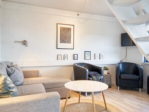 A modern living room with a sofa, armchairs, a coffee table, and a flat-screen TV mounted on the wall. - 5 Person Holiday Park Home in Gudhjem (Gudhjem)