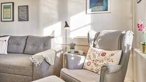A living room with a grey sofa, a grey armchair, and a small table with a lamp and a potted plant. There are two framed pictures on the wall. - 5 Person Holiday Park Home in Gudhjem (Gudhjem)