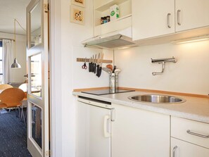 A modern kitchen with white cabinets, stainless steel appliances, and a window overlooking a dining area. - 5 Person Holiday Park Home in Gudhjem (Gudhjem)