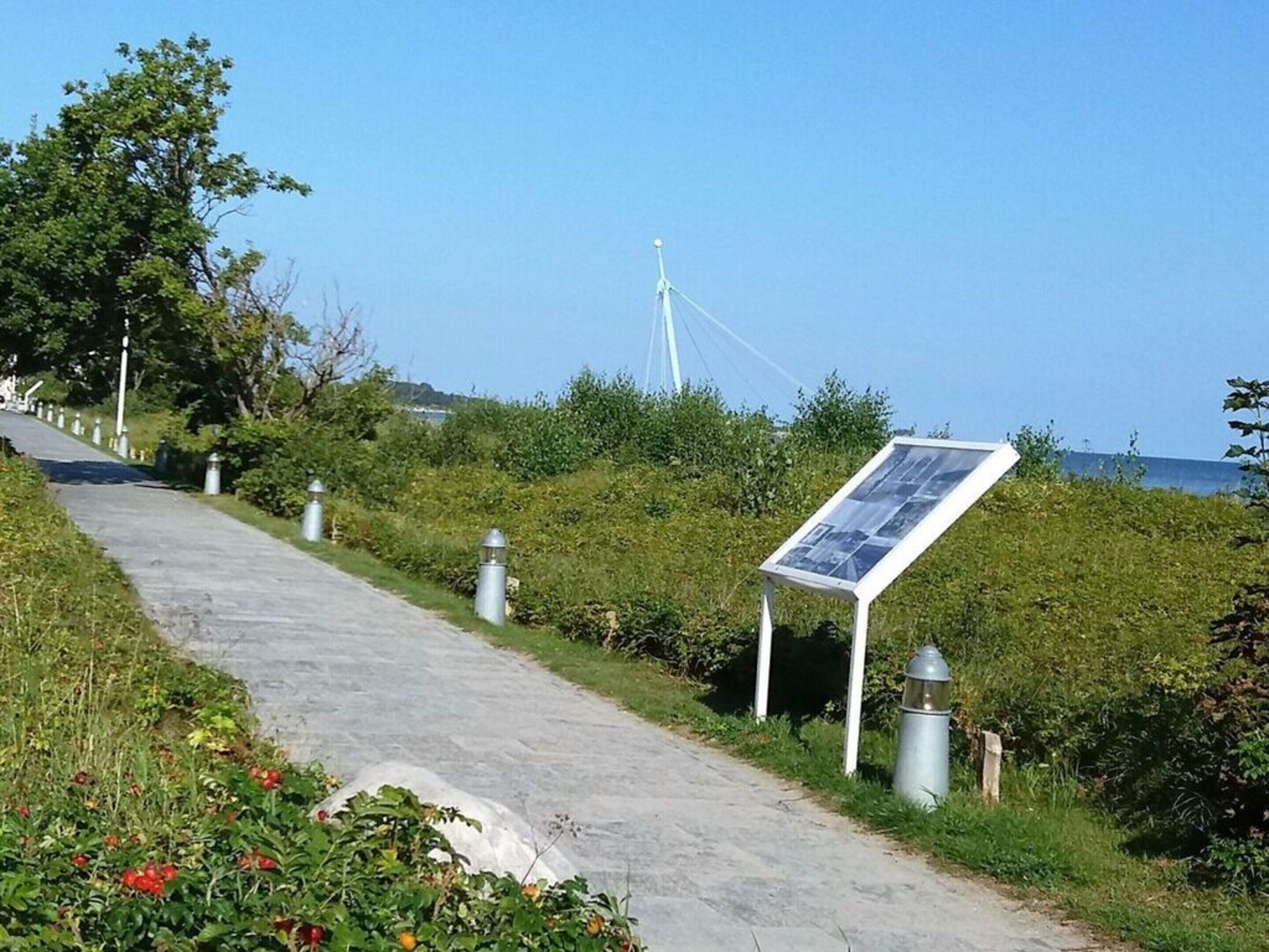 Een verhard pad met een bord, omgeven door groen en een windmolen op de achtergrond.