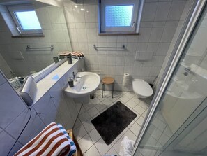 A bathroom with a sink, toilet, and shower. There are two windows providing natural light. - Holiday Apartment Achtern Diek (Hohwacht)