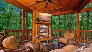 Une terrasse en bois avec des meubles en osier, une cheminée et un téléviseur.