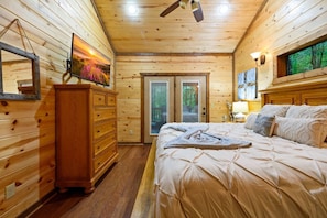Une chambre dans une cabane en bois, avec un lit, une commode et un tableau représentant un coucher de soleil.
