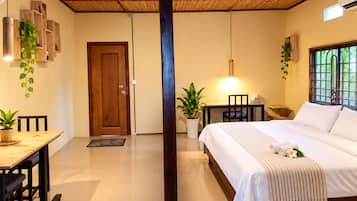 A hotel room with a bed, a desk, a chair, a dining table, and a potted plant.