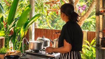 Una persona cocina al aire libre usando una estufa a gas, ollas y un lavamanos.