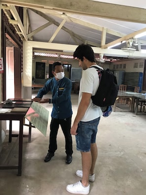Deux personnes se trouvent dans une pièce dotée d’un plafond haut, avec une table sur laquelle est posé un menu, et un tableau blanc en arrière-plan.