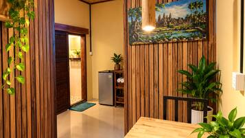 A room with wooden paneling, a painting of a landscape, a refrigerator, and a potted plant.