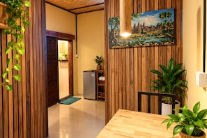 A room with wooden paneling, a painting of a landscape, a refrigerator, and a potted plant. - Madam Sokha Homesteading (Siem Reap)