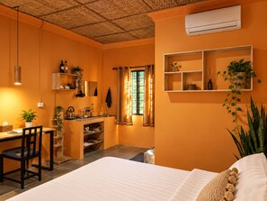 Una habitación con cama, escritorio, silla, zona de cocina y ventana con cortinas.