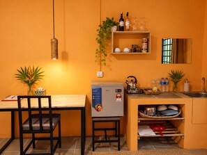 Cocina compacta con refrigerador, hervidor y lavamanos. Hay dos sillas y una mesita.