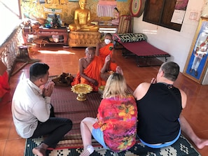A group of people in a room with a large golden statue, prayer mats, and religious artifacts. - Madam Sokha Homesteading (Siem Reap)