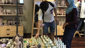 Een kamer met planken waarop diverse sculpturen staan en een tafel met meerdere kleine beeldjes.