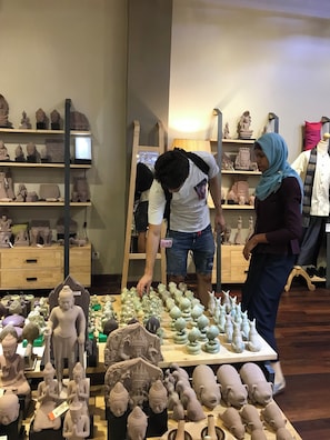 A room with shelves displaying various sculptures and a table with multiple small statues. - Madam Sokha Homesteading (Siem Reap)