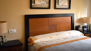 A hotel room with a large bed, two framed artworks on the wall, a nightstand with a lamp, and a bedside table with a bottle.