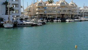 A marina with multiple boats docked, a white building with balconies, and a clear blue sky.