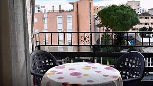 A balcony with a table and chairs, overlooking a cityscape with buildings and a tree.