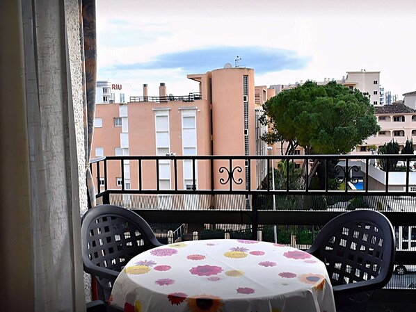 A balcony with a table and chairs, overlooking a cityscape with buildings and a tree. - Belvilla by OYO Apartment in Torremolinos (Torremolinos)