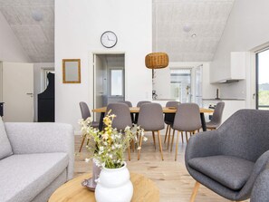 A modern living room with a sofa, a chair, a dining table with chairs, a vase with flowers, and a clock on the wall. - 5 Star Holiday Home in Romo (Rømø)
