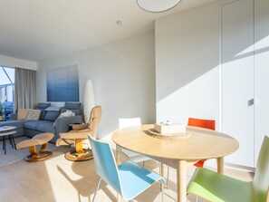 A modern living room with a sofa, chairs, a dining table, and a large window. - Exclusive Penthouse With Breathtaking 360deg View (Middelkerke)