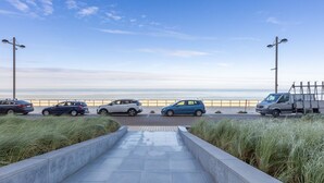 Un espace de stationnement avec des voitures et un fourgon, un chemin piétonnier pavé et une vue sur la plage.
