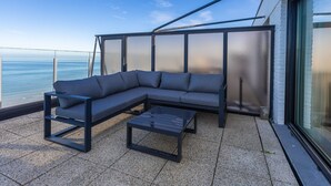 Un espace extérieur moderne, aménagé avec un canapé d’angle et une table basse, offrant une vue sur un plan d’eau.
