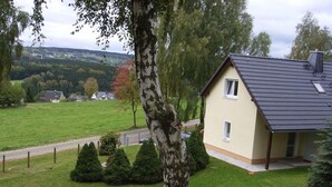 A house with a sloped roof, a small porch, and a view of a green field and distant houses. - Holiday Home Oertel Hausl (Marienberg)