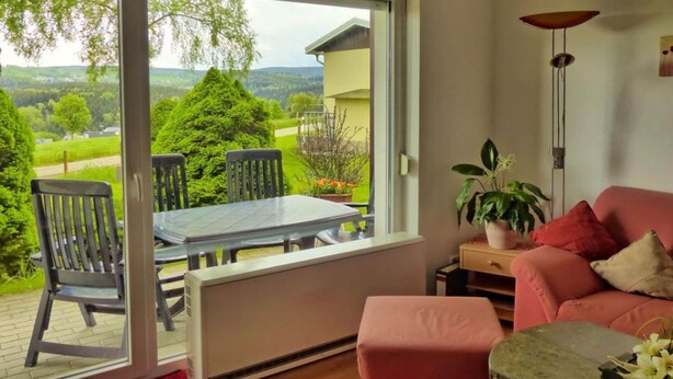 A room with a large window, a dining table with chairs, a pink sofa, a floor lamp, and a potted plant. - Holiday Home Oertel Hausl (Marienberg)