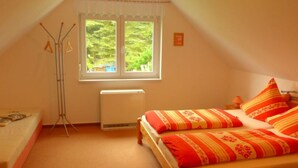 A small, cozy room with a sloped ceiling, a single bed with striped bedding, a radiator, and a window with a view of greenery outside. - Holiday Home Oertel Hausl (Marienberg)