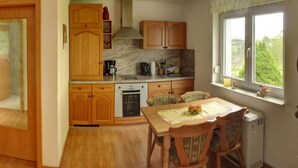 A kitchen with wooden cabinets, a built-in oven, and a dining area with a table and chairs. - Holiday Home Oertel Hausl (Marienberg)