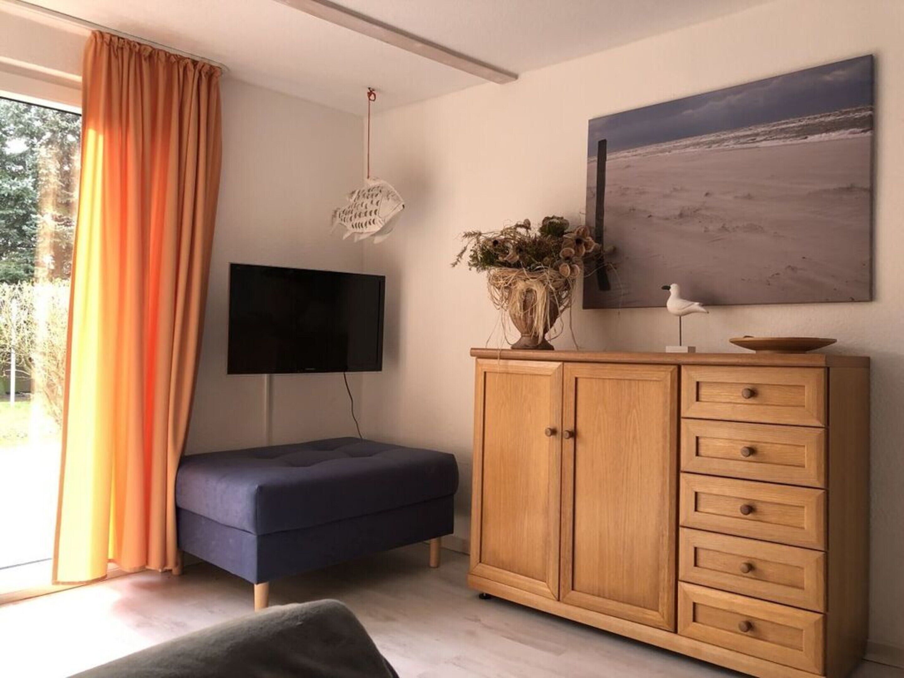 A modern living room with a dark blue sofa, wooden cabinet, and a flat-screen TV mounted on the wall.