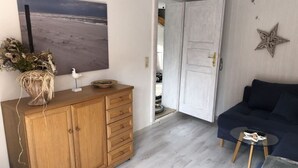 A living room with a wooden cabinet, a dark blue sofa, a glass coffee table, and a painting of a beach scene. - Fabian Comfortable Holiday Residence (Wieck auf dem Darss)